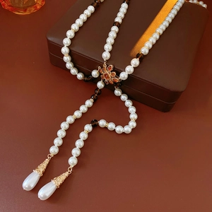 Detail of vintage teardrop pearl necklace with gold hollow charms on a leather jewelry box