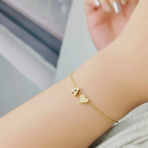 Detailed view of a gold delicate chain bracelet with an A-letter charm and a heart pendant