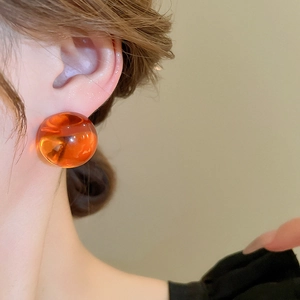Gros plan sur une boucle d'oreille sphérique en résine ambre portée avec un éclairage chaud