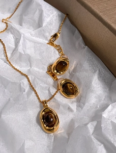 Detailed view of gold plated tiger eye stone necklace and earrings on white paper background