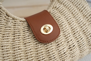 Detail of bohemian straw bag featuring caramel leather flap and golden oval twist lock