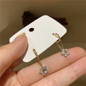 Macro detail of long gold floral earrings featuring shimmering zircon stones and delicate chains