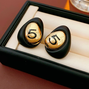 Macro detail of gold-plated drop earrings featuring a black number 5 on a jewelry box
