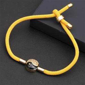 Close-up of yellow braided adjustable cord bracelet with golden Tai Chi Yin Yang charm