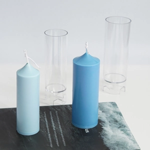 Clear plastic cylinder candle mold set with blue church pillar candles on a magazine