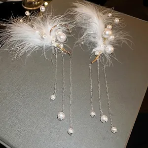 Elegant feather ear cuffs with pearls and gold metal tassels on grey background