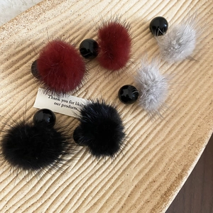 Détail de boucles d'oreilles pompons en bordeaux, gris et noir sur plateau en céramique
