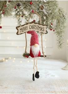 Detail of knitted Christmas gnome on wooden swing hanging from a pine tree branch