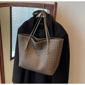 Detailed view of a brown woven tote bag hanging on a black wool coat in natural light
