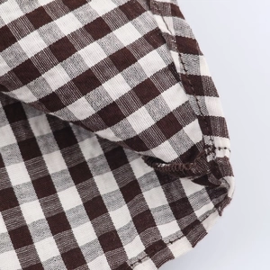 Close-up of brown plaid fabric texture and professional overlock stitching on the shirt