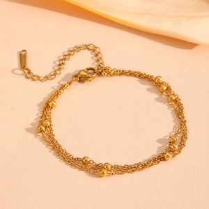 Detail of gold multilayered steel bracelet featuring bead accents and lobster clasp closure