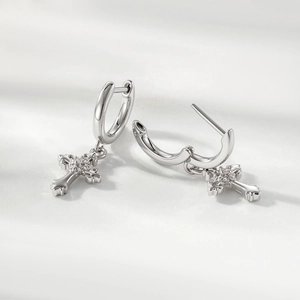 Polished silver iris cross hoop earrings with clear gemstone on soft fabric background