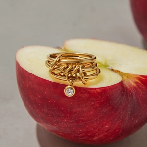 Detailed macro view of gold multi-layered rings with zircon pendant on a fresh apple