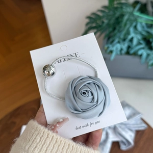 Detail of gray silk rose hair tie with engraved metal bead on a display card
