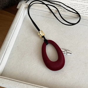 Detail of burgundy flocked resin pendant with gold bead on a black cord necklace