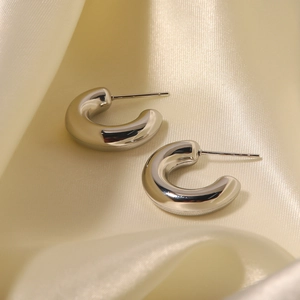 Close-up of silver C-shaped hollow earrings resting on beige silk fabric background