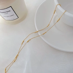 Close-up of a minimalist S925 sterling silver gold beaded necklace on a white ceramic cup