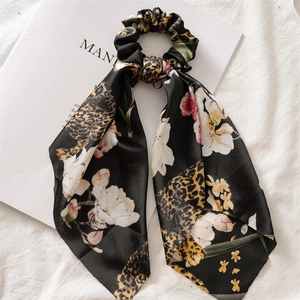 Detailed view of black leopard and floral print satin scrunchie on fabric backdrop