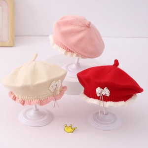 Three knitted baby berets with lace ruffles and bows in pink, beige and red colors