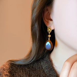Modèle portant des boucles d'oreilles goutte d'eau dorées avec pierres en résine brun-bleu