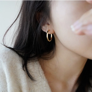 Detailed view of medium-sized golden hoop earring worn by a model in beige knitwear