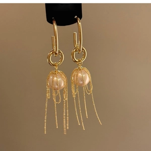 Detail of gold tassel drop earrings featuring cage-wrapped pearl and delicate metal chains