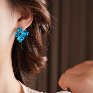 Close-up of model wearing blue geometric crystal stud earrings in a modern floral cluster