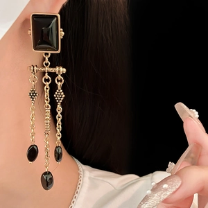 Detail of vintage gold earrings with black square stone and long tassel on a model