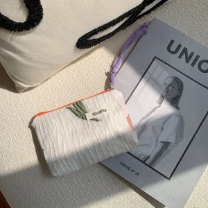 Detailed view of the cream knitted fabric pouch with orange zipper and green leaf embroidery