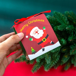Hand holding red square paper Christmas gift box with Santa illustration and Merry Christmas text