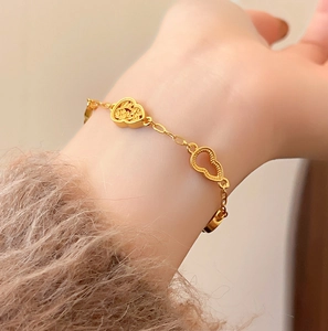 Vergoldetes Armband mit Herz- und Flaschenkürbis-Anhängern am Handgelenk mit Pelzärmel