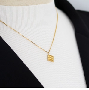Macro detail of golden square chocolate pendant with 3x3 grid texture on fine chain