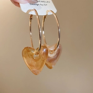 Detail of amber acrylic heart pendant on gold hoop earrings with marble texture