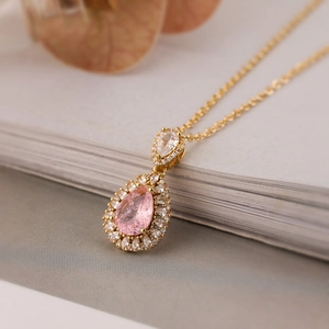 Close-up of a pear-cut pink zircon pendant surrounded by white crystals on a gold chain