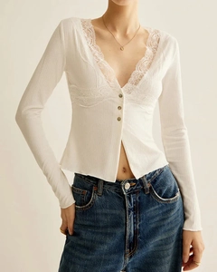 Detail of white long-sleeve crop top with delicate lace trim and V-neck button design