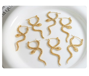 Macro shot of gold snake-shaped earrings showing detailed scale textures on a ceramic tray