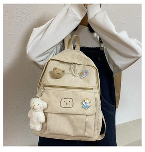 Detalle de la mochila de pana crema con bordado de oso y distintivos decorativos