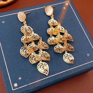 Elegant gold hollow leaf tassel earrings with opal studs on dark blue jewelry box
