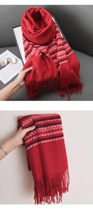 Detail view of a red knit scarf with fringe and tricolor stripes on a gray sofa background