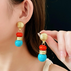 Detail of vintage gold earrings with red beads and blue turquoise stones on a model