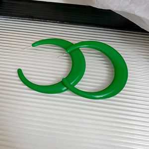Close-up of chunky green C-shaped acrylic hoop earrings with a glossy polished finish