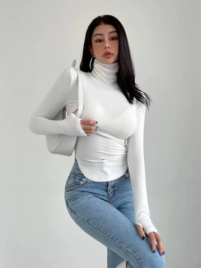 Top bianco attillato a maniche lunghe con collo alto e jeans per un look alla moda