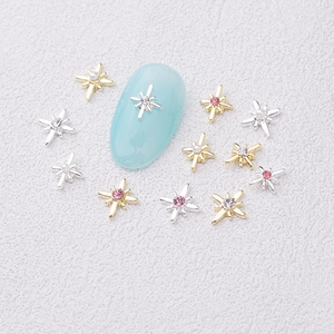 Macro view of compass star nail charms with pink rhinestones and pearls on a blue nail