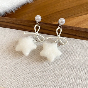 Detail of white velvet star and ribbon bow earrings with pearl stud on beige fabric