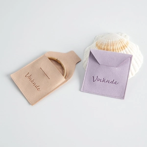 Vista plana de bolsas de joyería de microfibra en crema y lavanda con una pulsera de oro