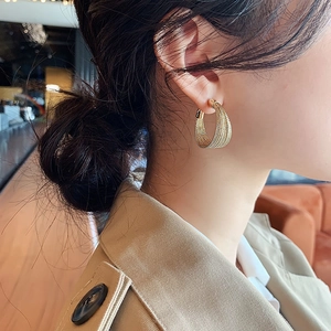 Close-up of golden multi-layer braided texture hoop earrings on a female model