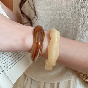 Close-up of irregular acrylic bangles in amber and beige worn by model over a book