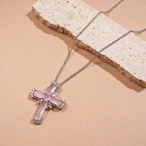 Vue détaillée du pendentif croix en argent avec pierres roses sur fond de pierre beige
