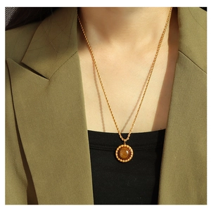 Detail of tiger eye pendant on a gold twisted rope chain worn by a fashion model