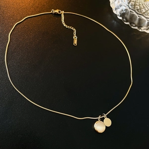 Detailed close-up of golden snake chain with opal pendant on black leather background